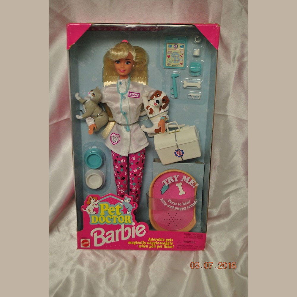 Pet Doctor Barbie inside her box. Dressed in pink leggings and a vet coat with vet accessories including a cat and dog
