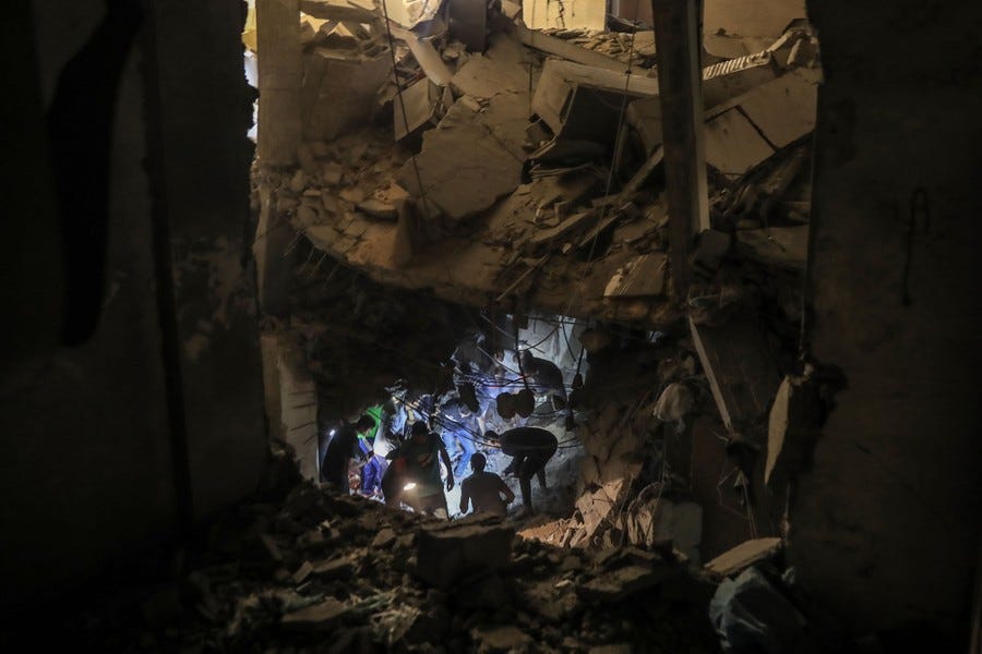 A view looking into the rubble of a destroyed building, where several people using flashlights search inside