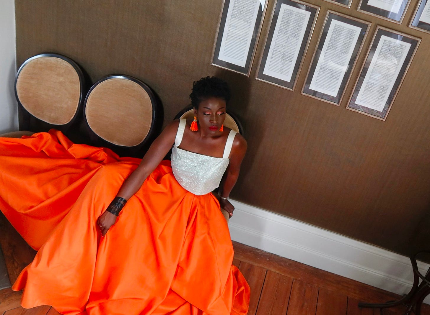 Lovette Jallow posed in orange and white, leaning forward as if mid-thought, radiating quiet determination.