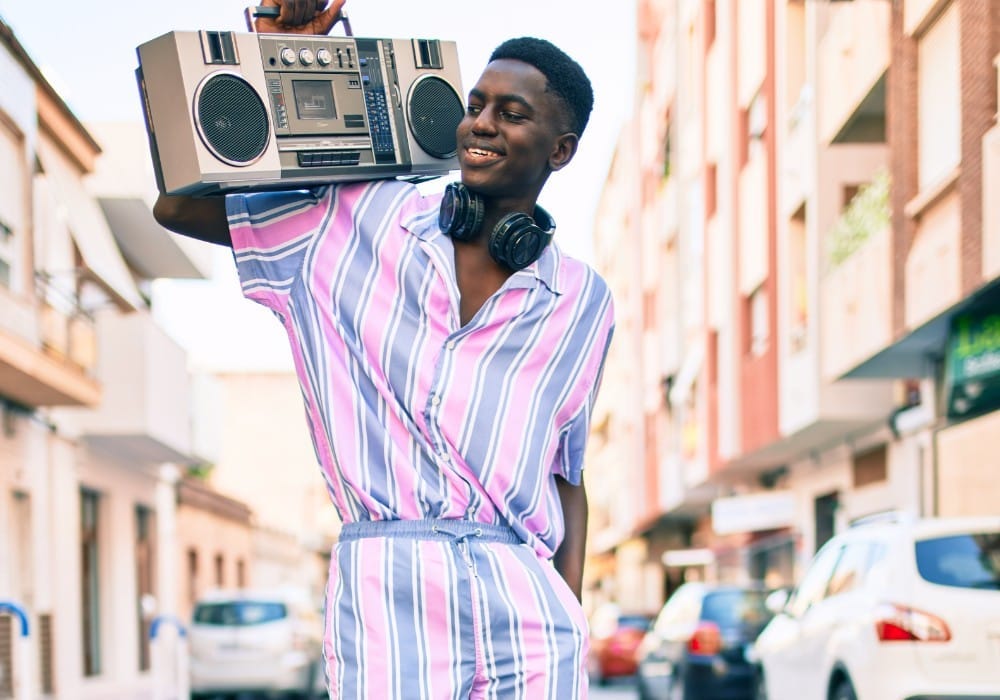 Vintage 80s photo of black man smiling in a colorful outfit with boom box on his shoulder