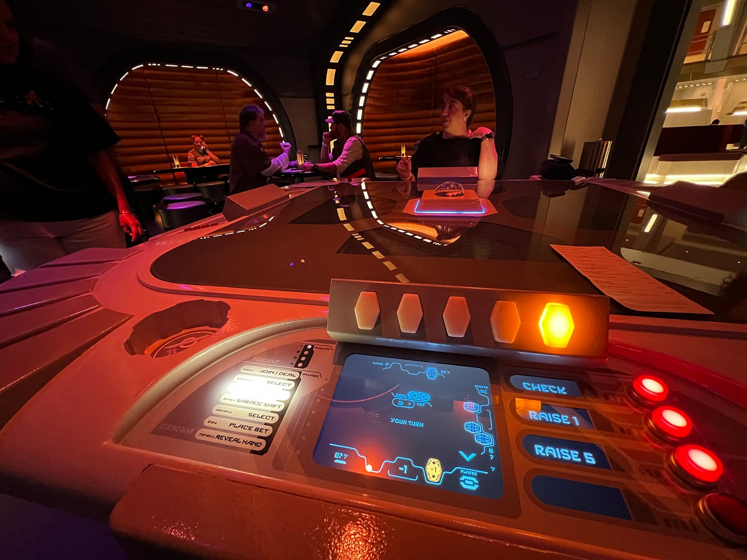 A gaming table with computer screen built in, with buttons for Check, Raise 1, and Raise 5 like in poker