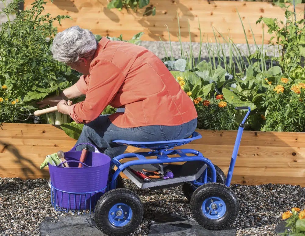 This image provided by Gardener’s Supply Company shows a woman gardening in a raised bed while seated on a Deluxe Tractor Scoot, one of many available products designed to make gardening easier. (Gardeners.com via AP)