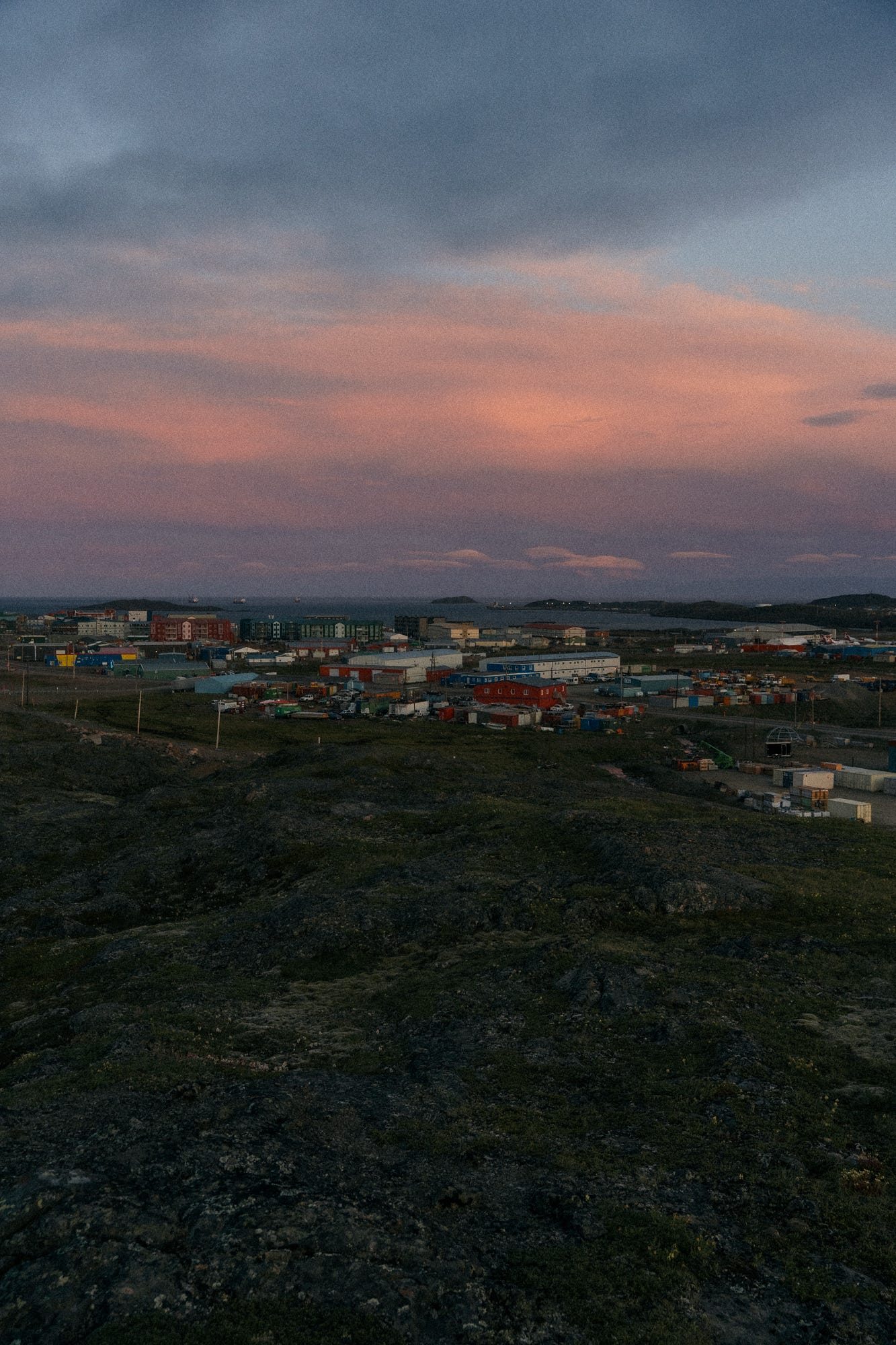 A pink and blue sky with light clouds over the town of Iqaluit and the ocean in the background.