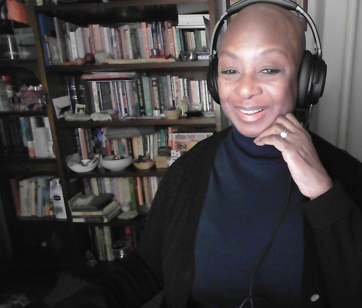 Selfie of Eva Yaa Asantewaa in her home office in front of a bookcase. She's wearing a dark sweater and headphones and smiling at the webcam.