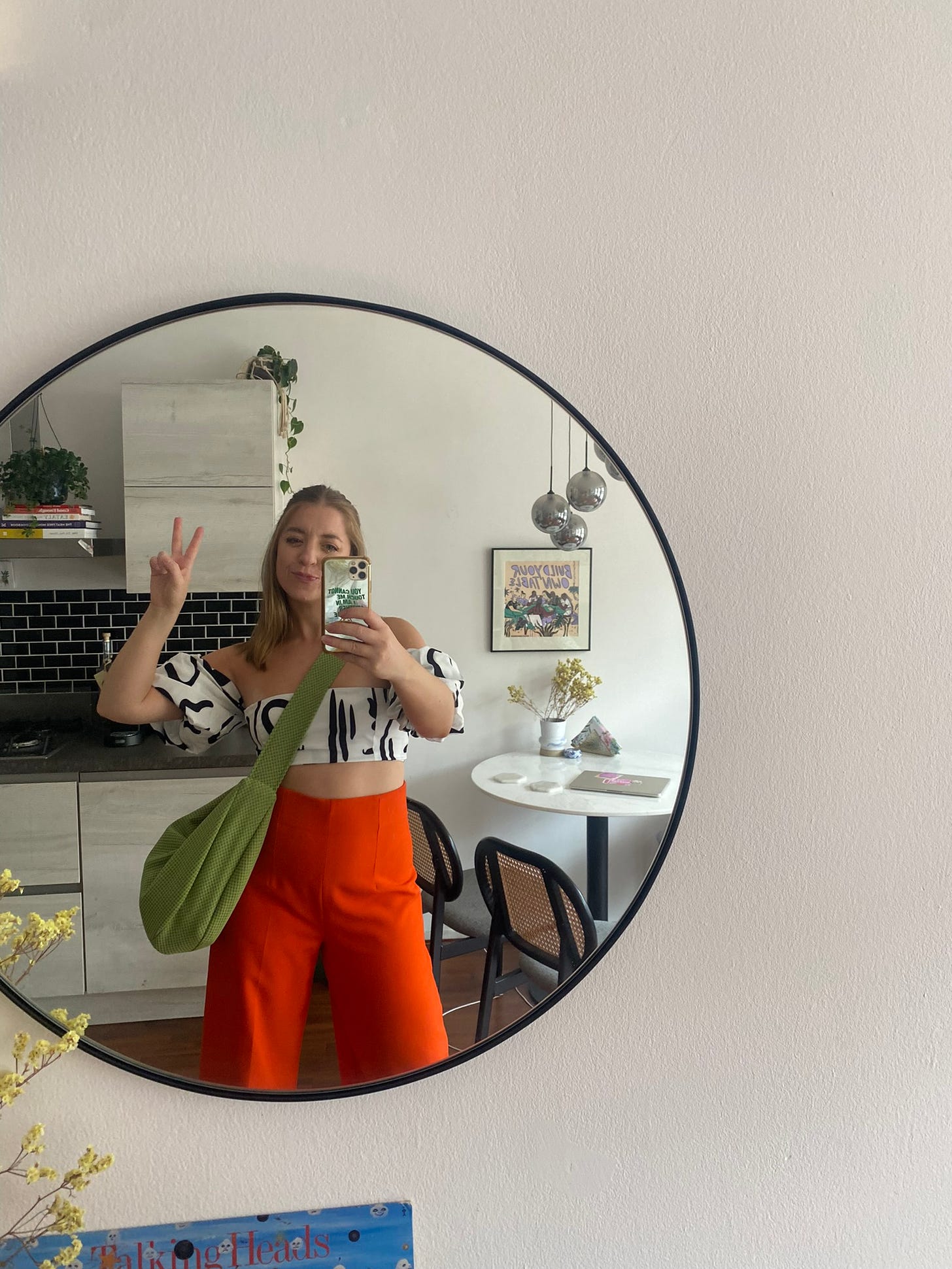 Kelly in orange pants, a black and white crop top, and green crossbody bag.