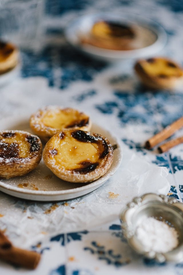 Fotografia a colori dei pasteis de nata: piccoli dolcetti ripieni di crema gialla, bruciacchiati ai bordi e spolverati di zucchero a velo.