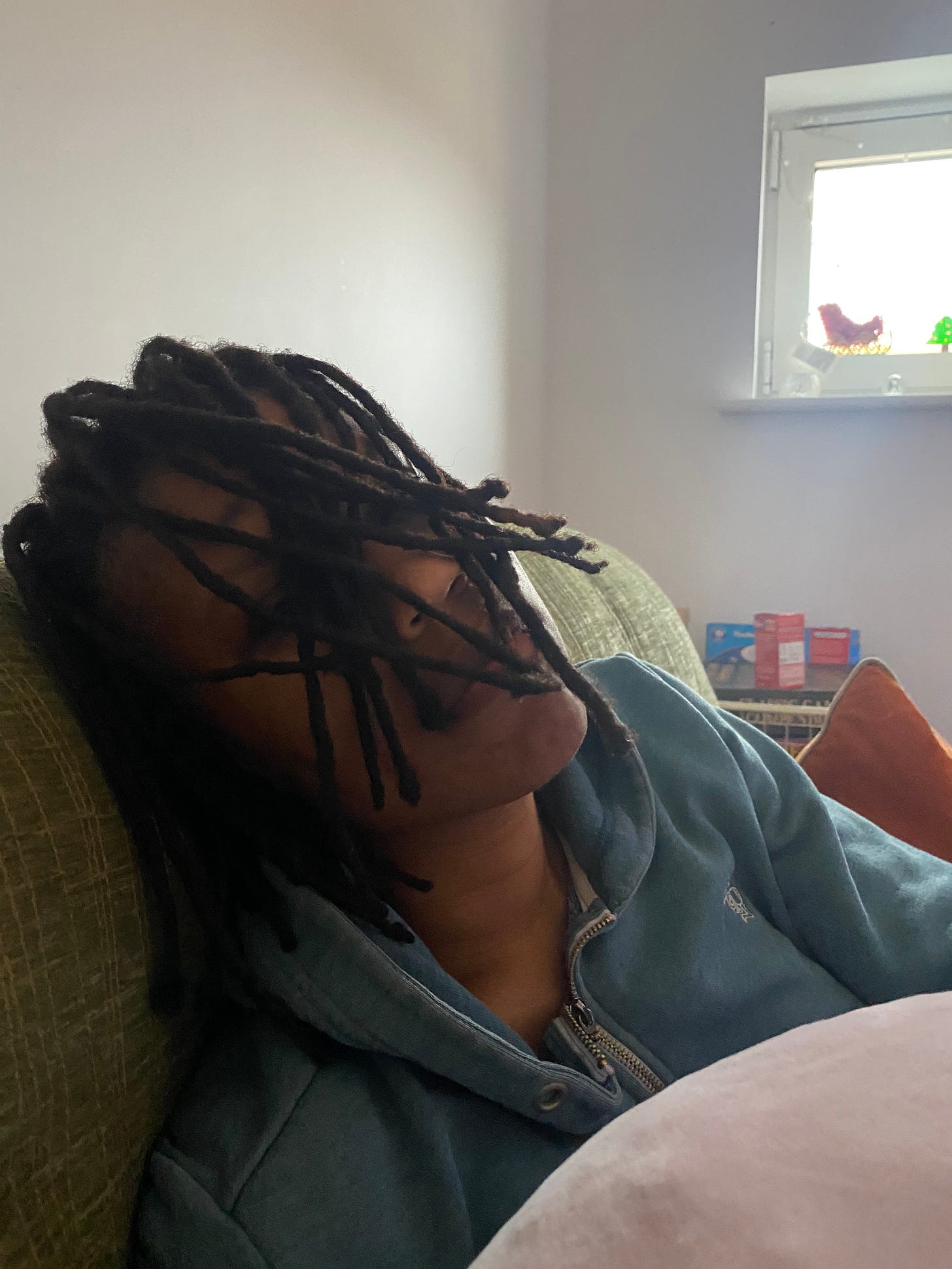 Sandra has black locs covering their face while sitting towards the camera in a blue jumper 