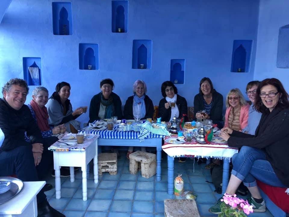 A group of 10 people sit in a blue-walled cafe drinking tea and smiling