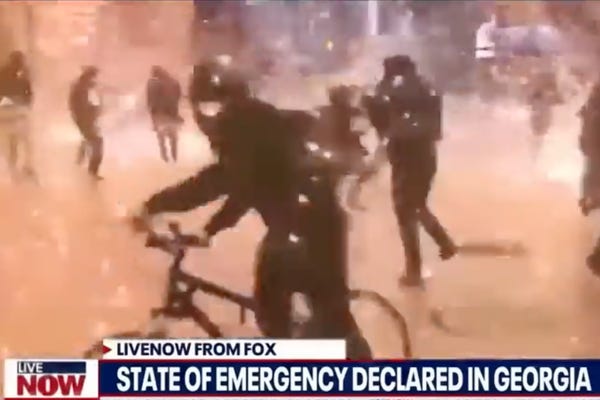 A still from a news report shows protesters clashing with the police over a chyron that says “Live Now From Fox” and “State of Emergency Declared in Georgia.”