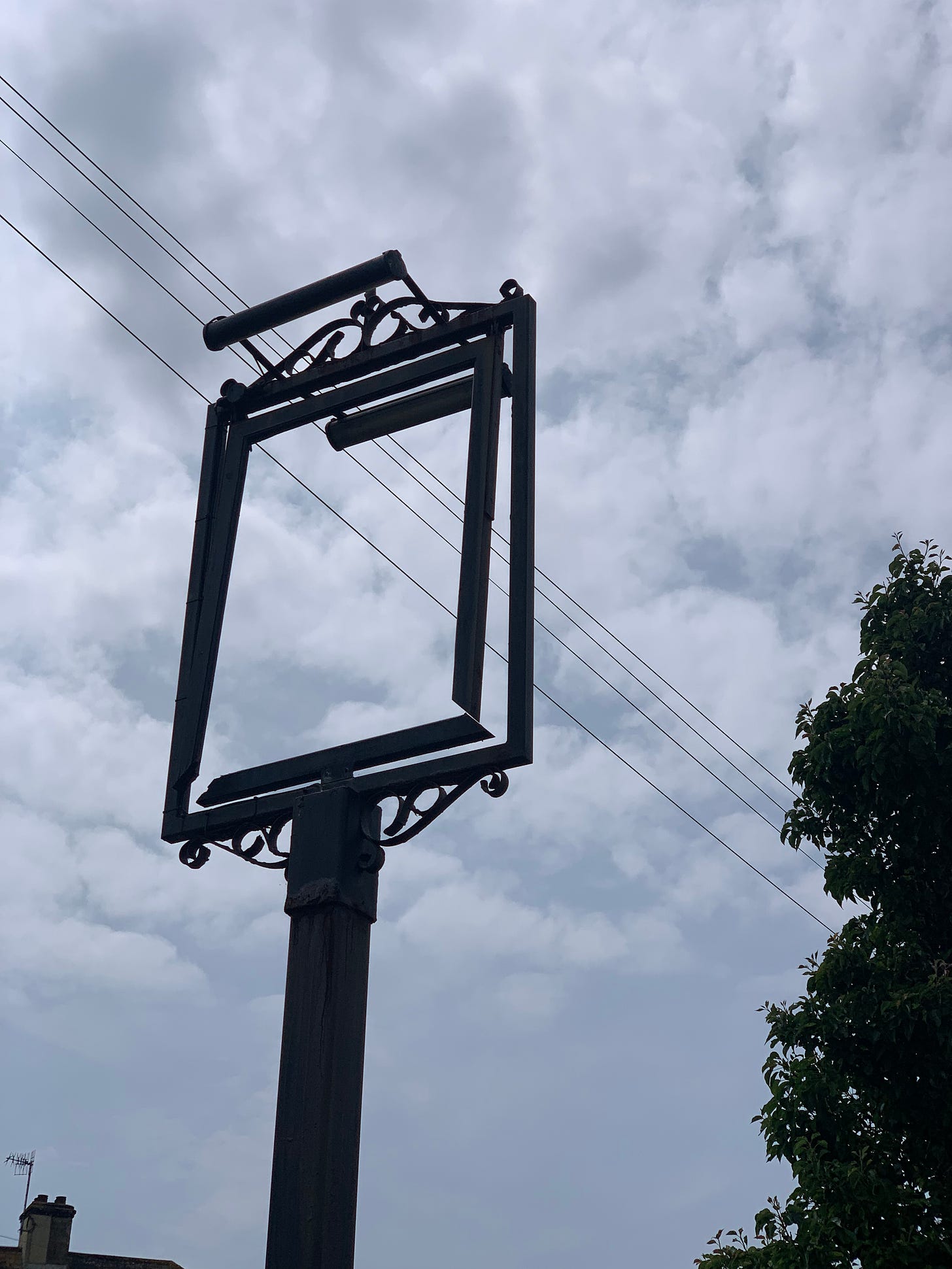 A photo of an empty wrought-iron sign frame against a cloudy sky with power lines running behind it 