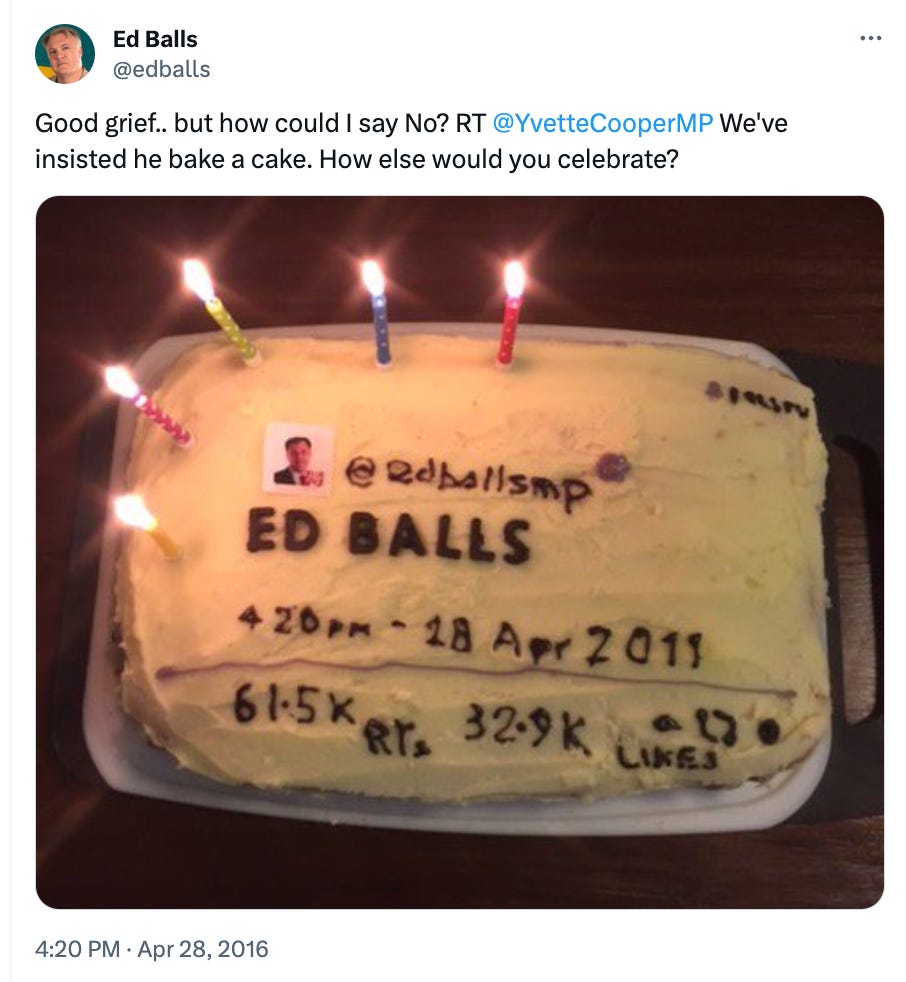 Tweet from Ed Balls dated April 28, 2016, with an image of a homemade cake. The cake has white icing and is decorated with various texts and numbers in icing that mimic a tweet format. On the upper left, a printed photo of a Twitter profile picture with the handle @edballsimp is placed. Below it, in large letters, is the name 'ED BALLS'. Underneath, a mock tweet is recreated with icing, showing a timestamp '4:20 PM - 18 Apr 2011', and Twitter engagement numbers '61.5K Retweets 32.9K Likes', along with small emoticons. The cake has five lit birthday candles of different colors