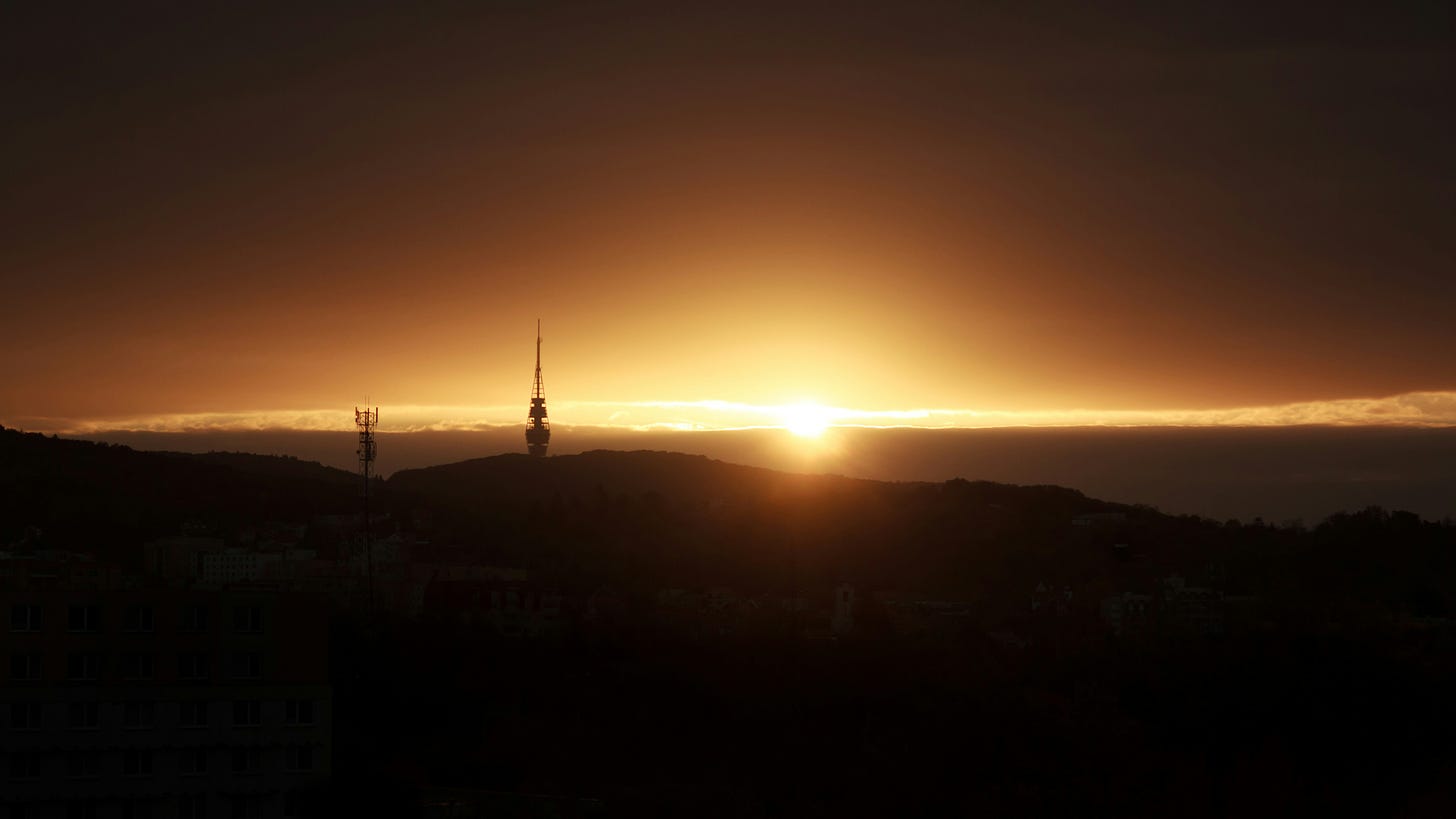 The sun rises at daybreak over a hill. Two spires can be seen in the foreground.