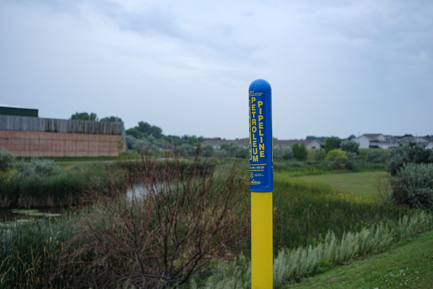 A blue and yellow signing denoting a petroleum pipeline along a retention pond in Bismarck North Dakota. 