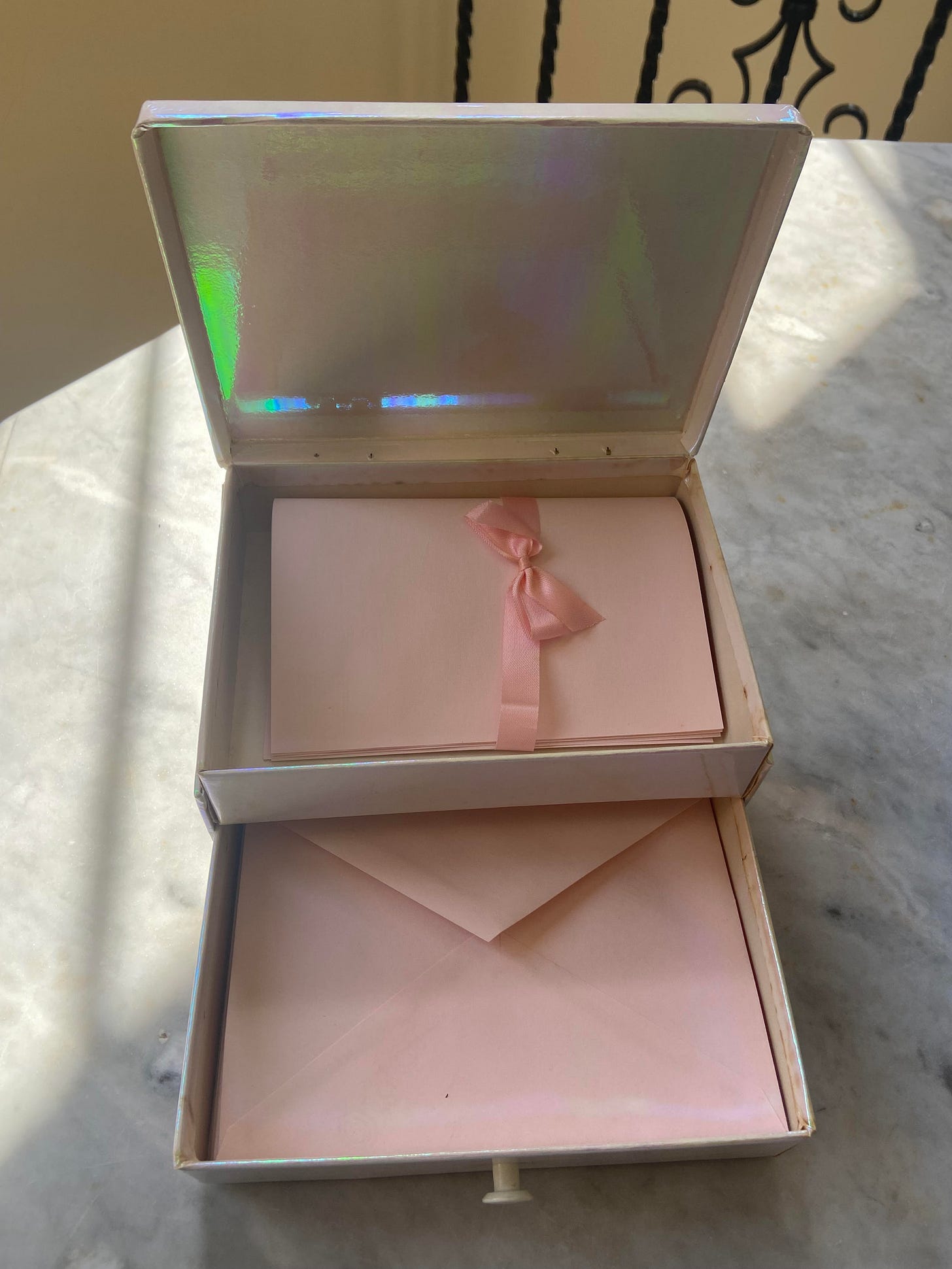 Photo of a small opened pink box with an open drawer. The top part has folded blank sheets of pink paper gathered together with a pink ribbon tied in a bow and the drawer has a stack of small pink envelopes Photo of a small opened pink box with an open drawer. The top part has folded blank sheets of pink paper gathered together with a pink ribbon tied in a bow and the drawer has a stack of small pink envelopes