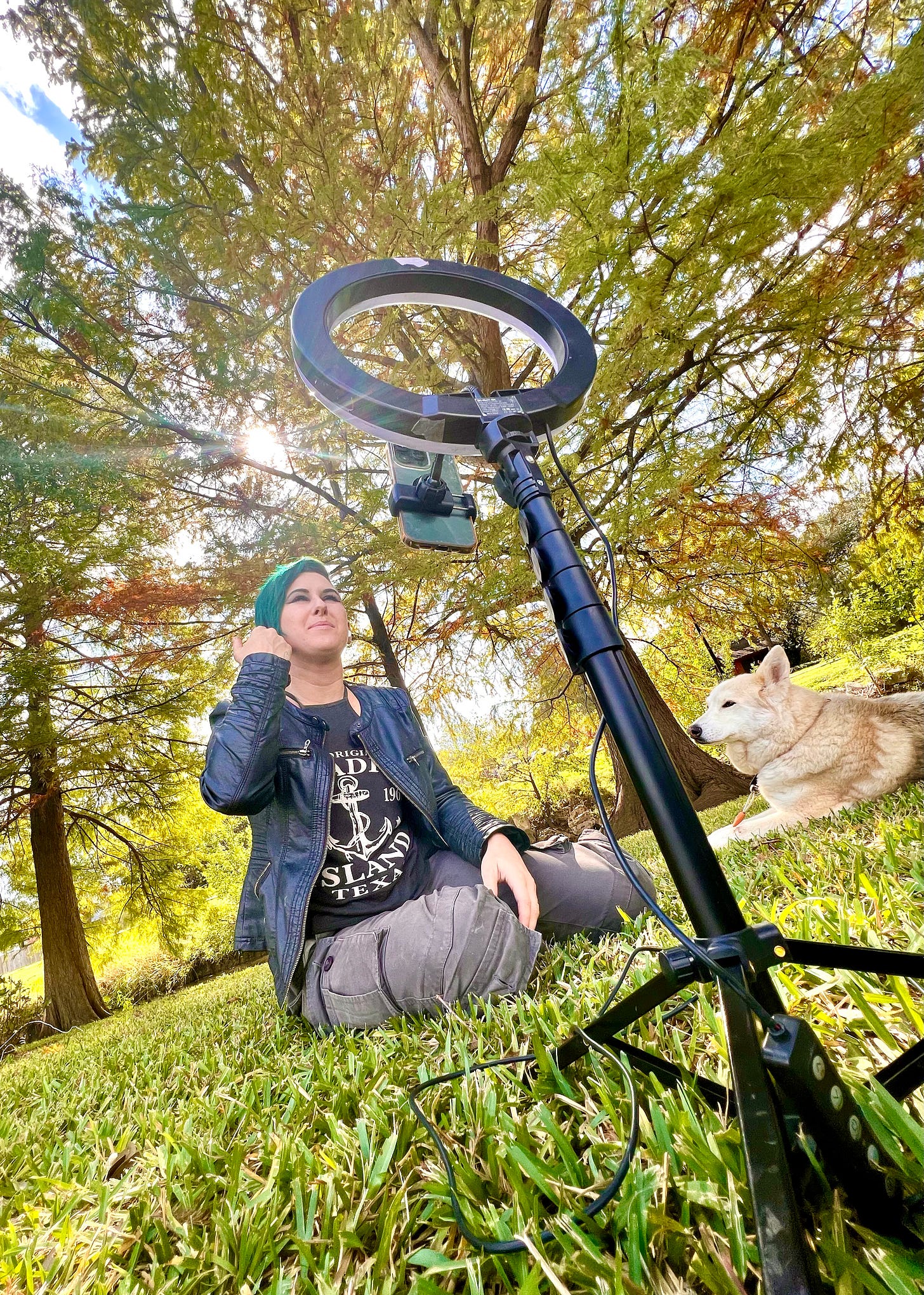 Lyric and Rocky, sitting outside under the trees together, as Lyric is on a Zoom call with another Autistic Person they met through their blog.