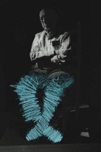 Dr. Gordon Warme, an older man, on a black background, with blue painted scribbles lighting up his legs Dr. Gordon Warme, an older man, on a black background, with blue painted scribbles lighting up his legs