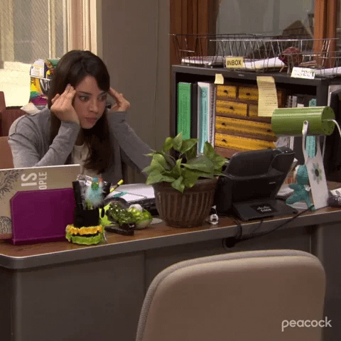 A woman sits at an office desk holding her head