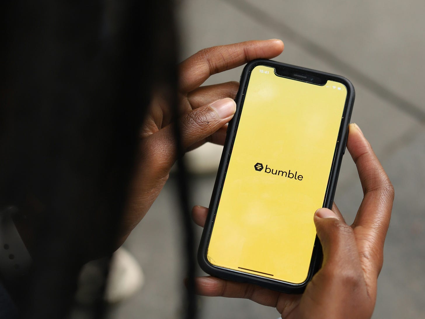 Schwarzer Mensch schaut auf Handy-Bildschirm, auf dem das gelbe Bumble-Logo zu sehen ist.