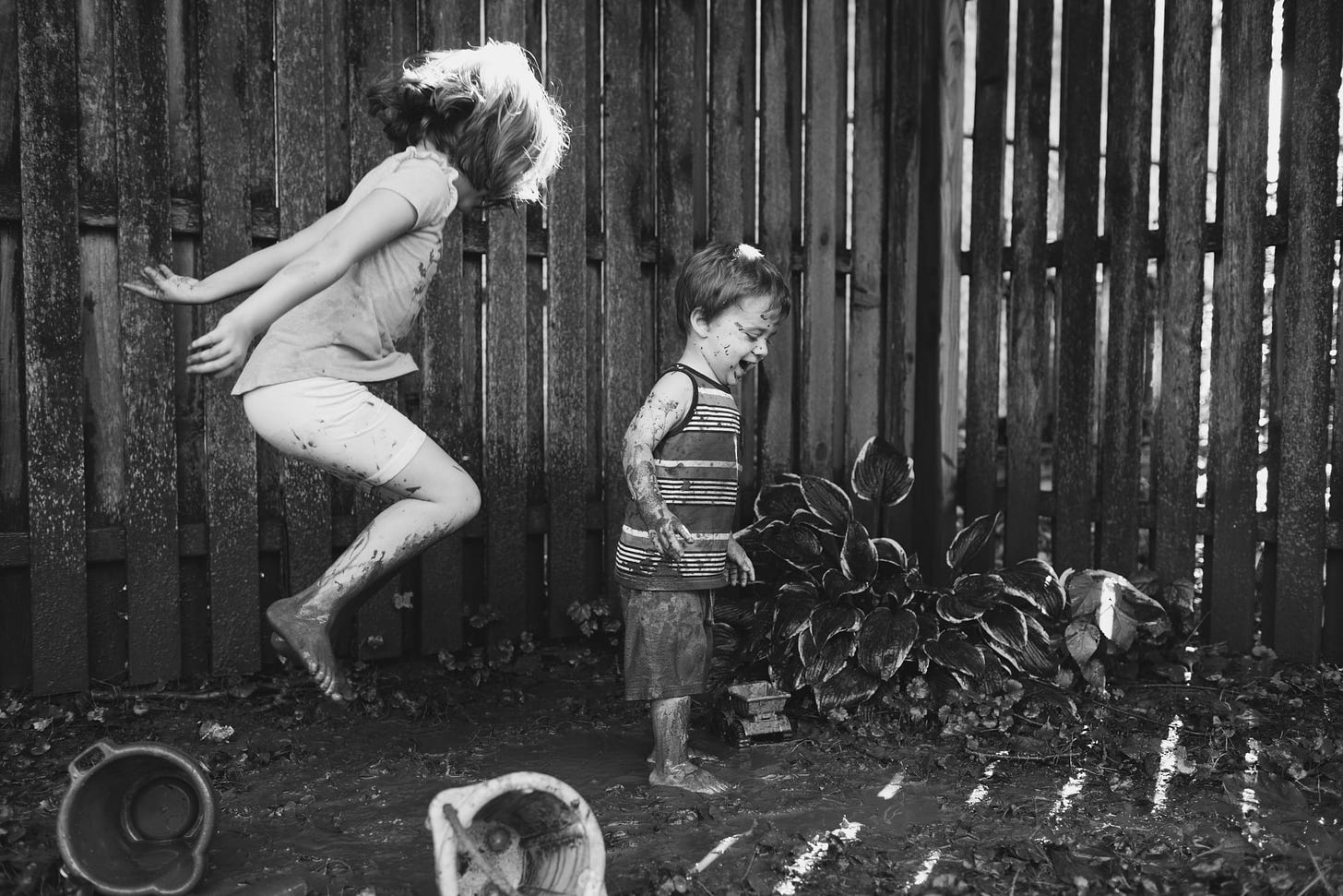 A black and white of siblings jumping in mud in their backyard.