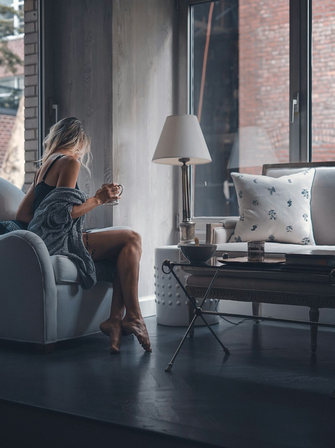 woman sitting on gray sofa chair holding mug woman sitting on gray sofa chair holding mug