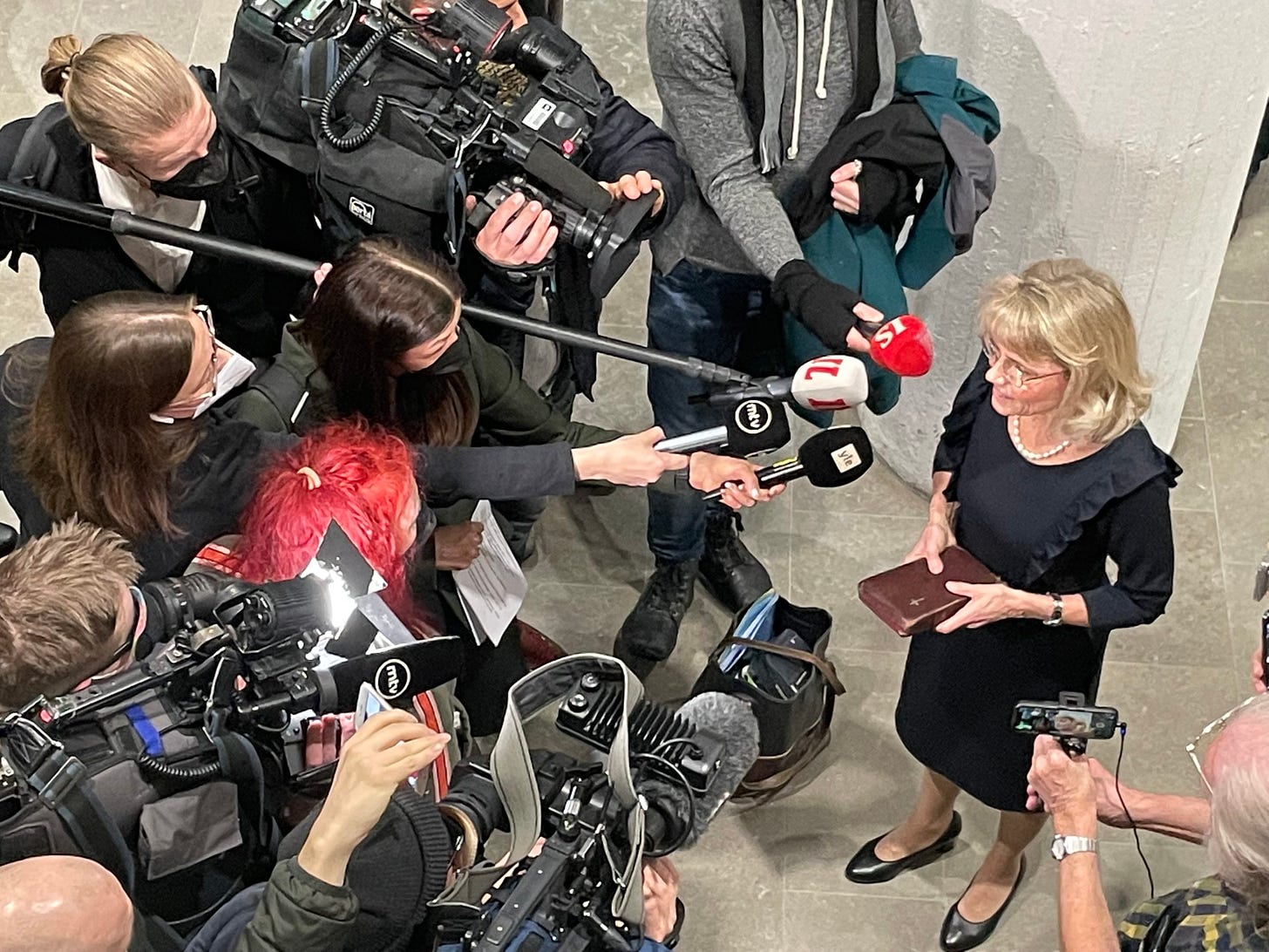 Woman holding a Bible faqces a group of TV journalists holding cameras and microphones.