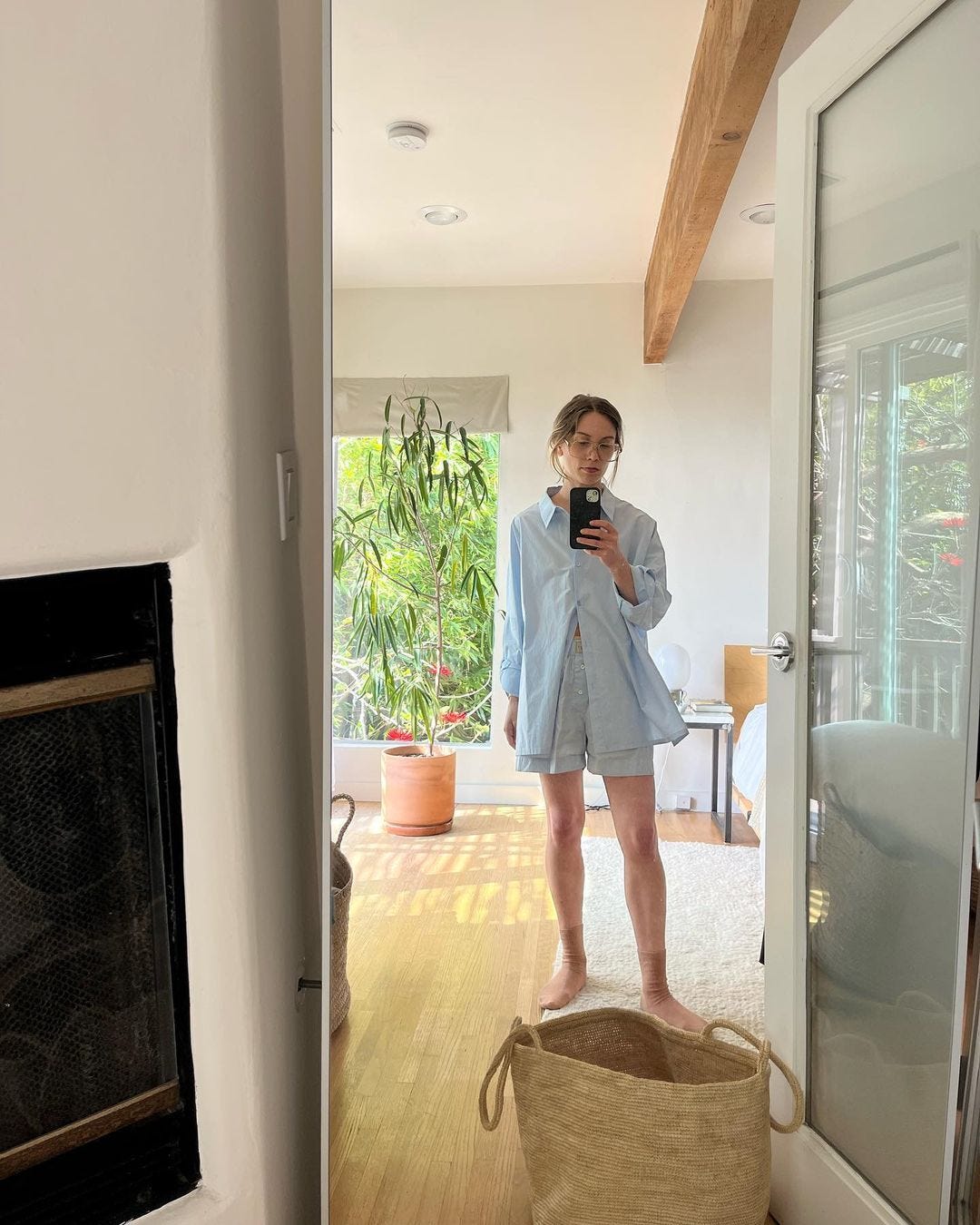 Woman taking a photograph of her reflection in the mirror in a sunlit room.