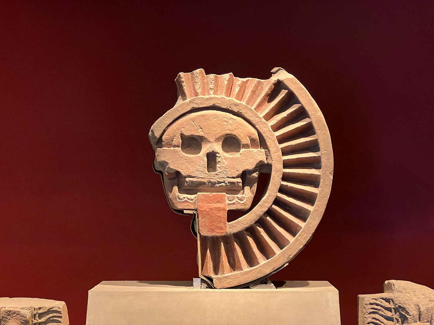 A light colored stone disk representing a skull and pleated headdress A light colored stone disk representing a skull and pleated headdress