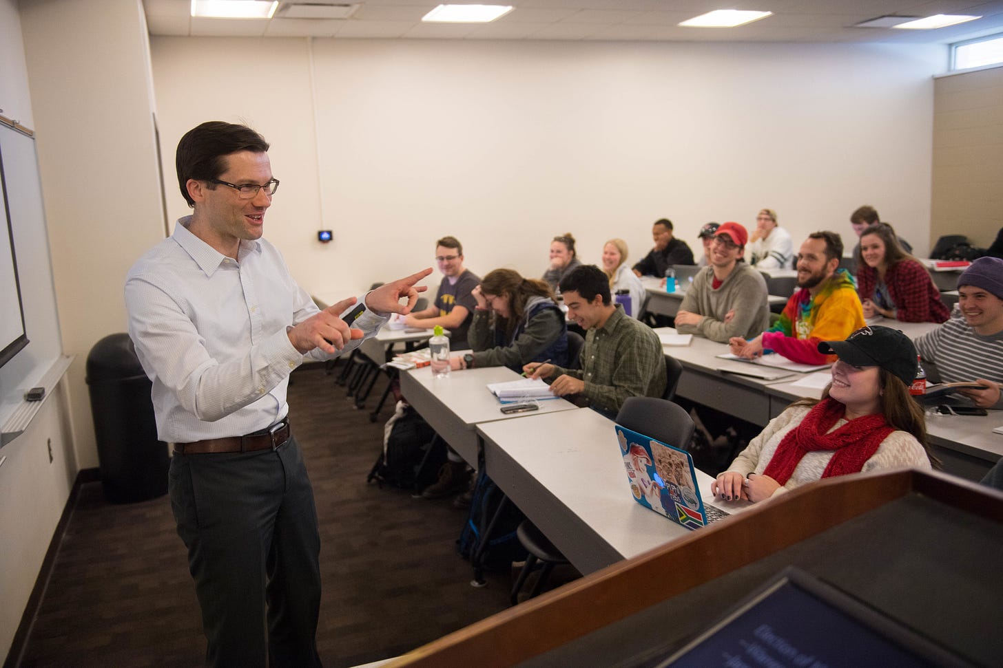 A UM instructor gestures at the head of a classroom as students laugh and smile