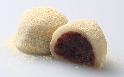 On the left, a dome-shaped white mochi ball covered with yellowish soy powder. On the right, the cross section of the same dumpling that shows red bean paste in the middle.