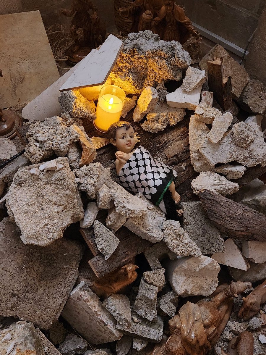 a Nativity scene, the Christ child wrapped in a keffiya and surrounded by broken concrete rubble and candles
