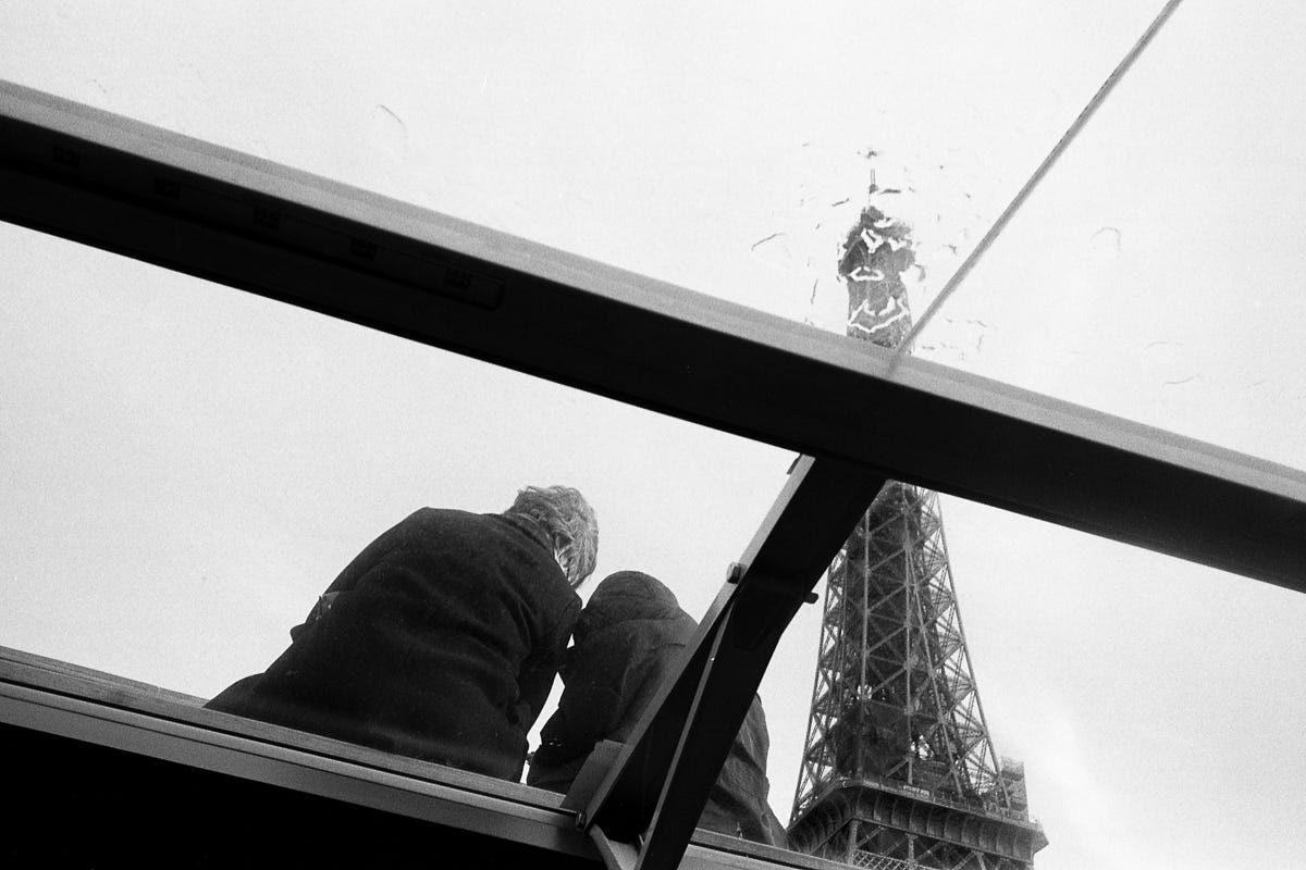 A couple seen from behind and below through a barge glass roof leaning in to each other with the Eiffel Tower beyond them