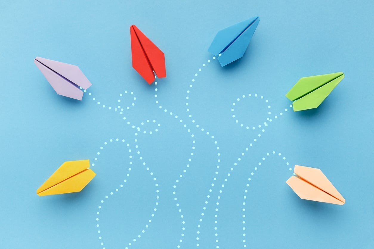 Multicolored paper airplanes flying in different directions on a blue background.