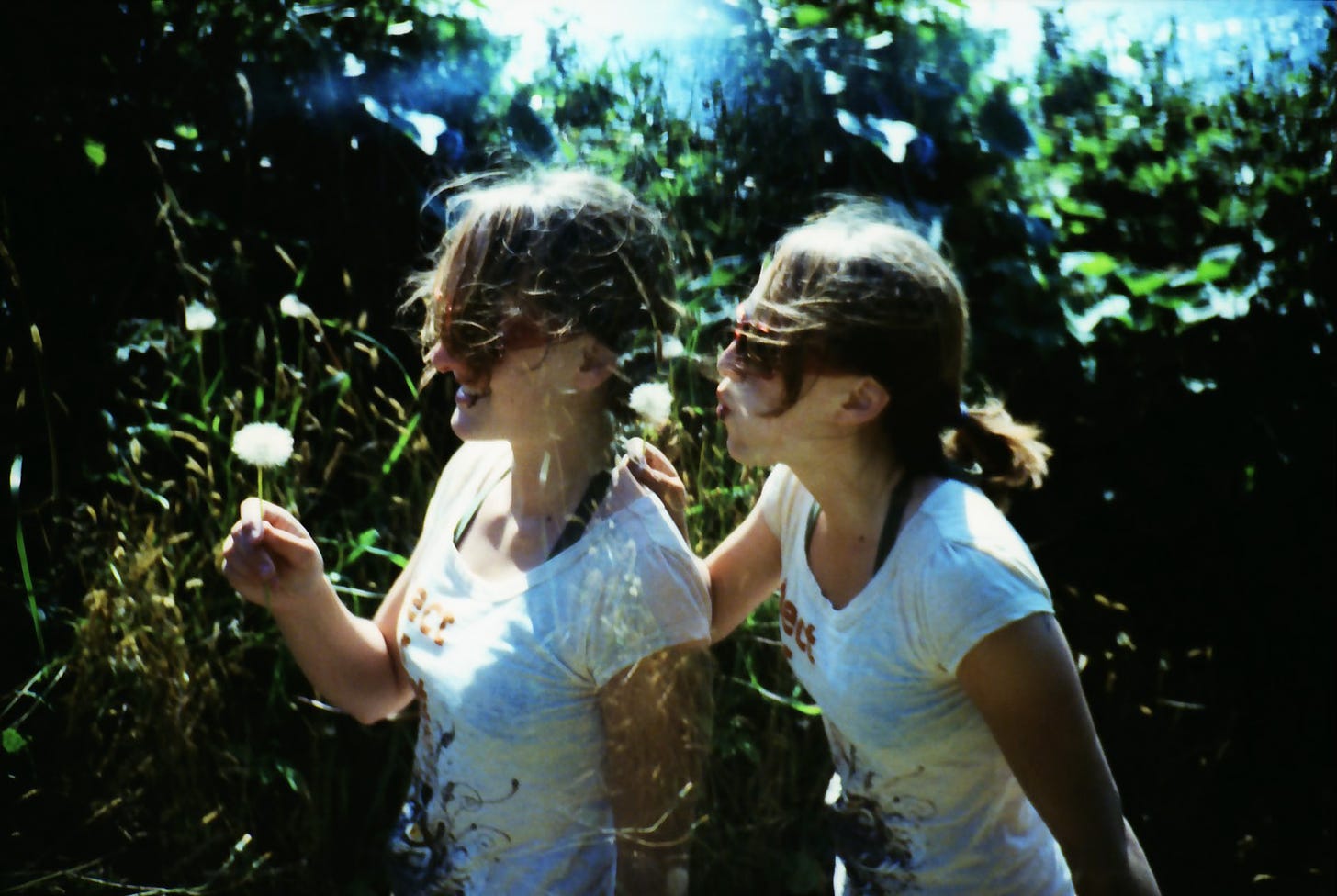 A double exposure shows two Sarahs, one holding a dandelion, and the other blowing on a dandelion.