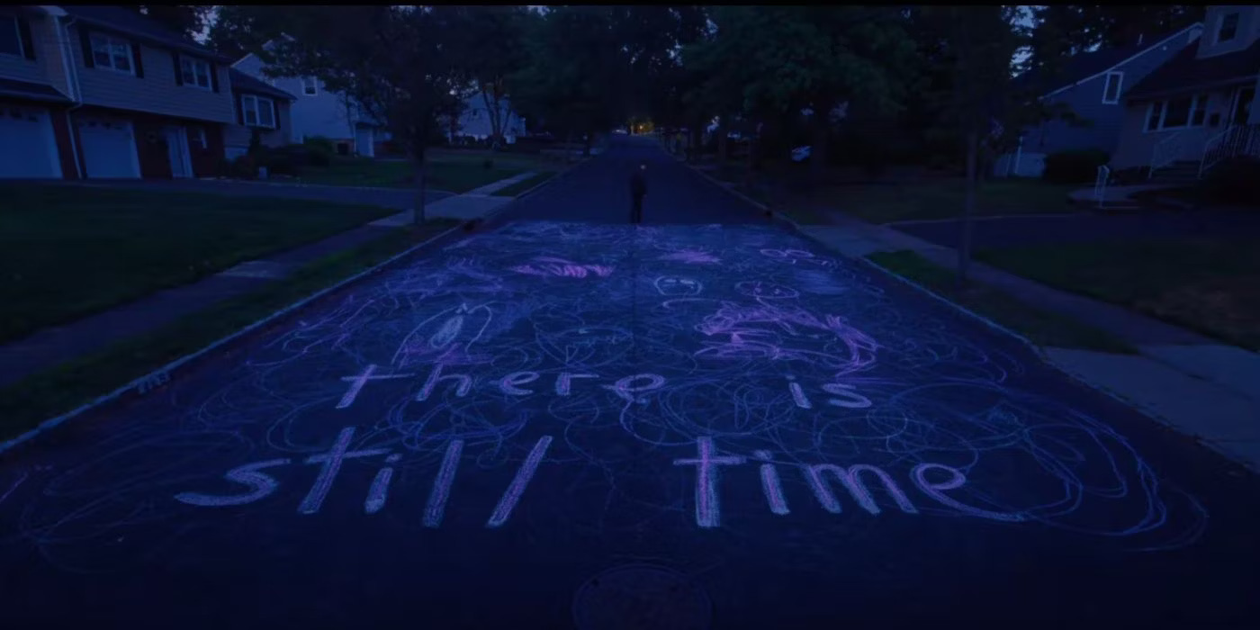 A suburban street after dark, with "there is still time" written in glowing pink paint surrounded by doodles