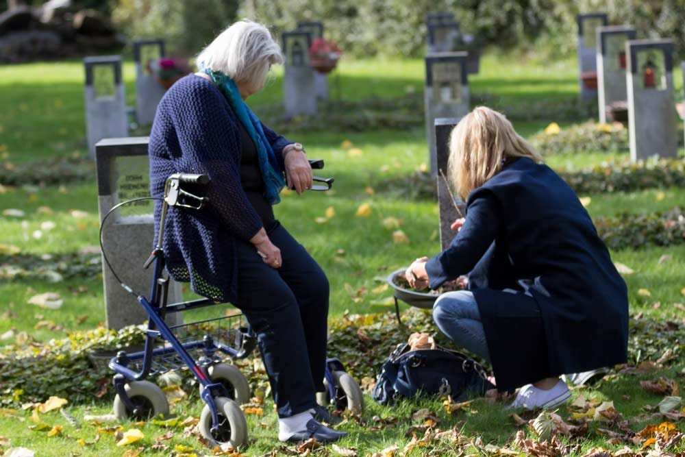 Senior woman sitting on her mobility scooter while visiting a cemetary with her adult daughter.