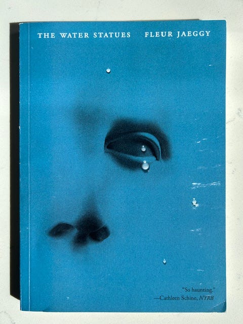 A blue cover has a partial face, an eye and a nose, and a tear falls from the eye. Text reads The Water Statues Fleur Jaeggy