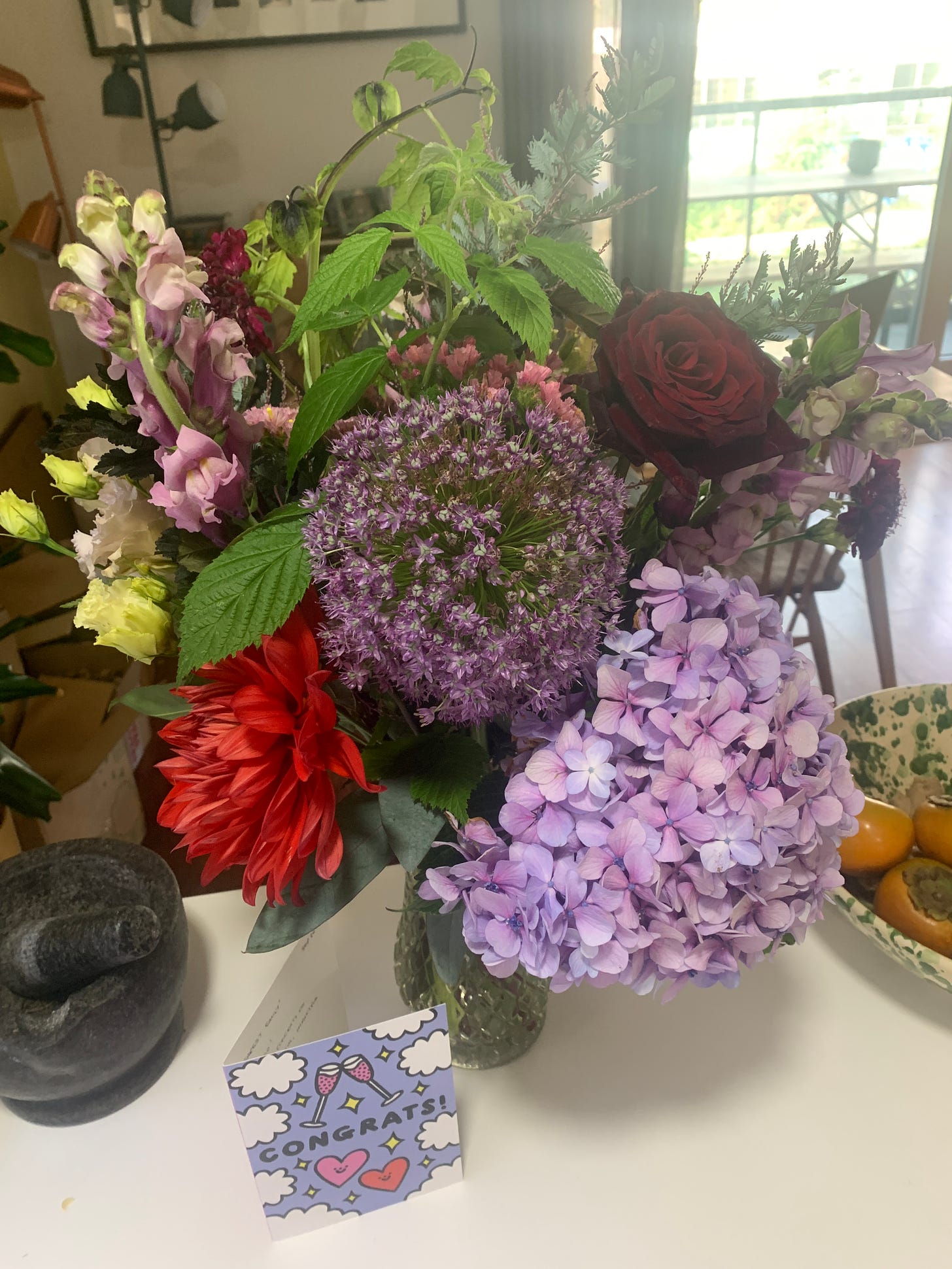 A bunch of flowers on a kitchen counter, they are mostly red and lilac