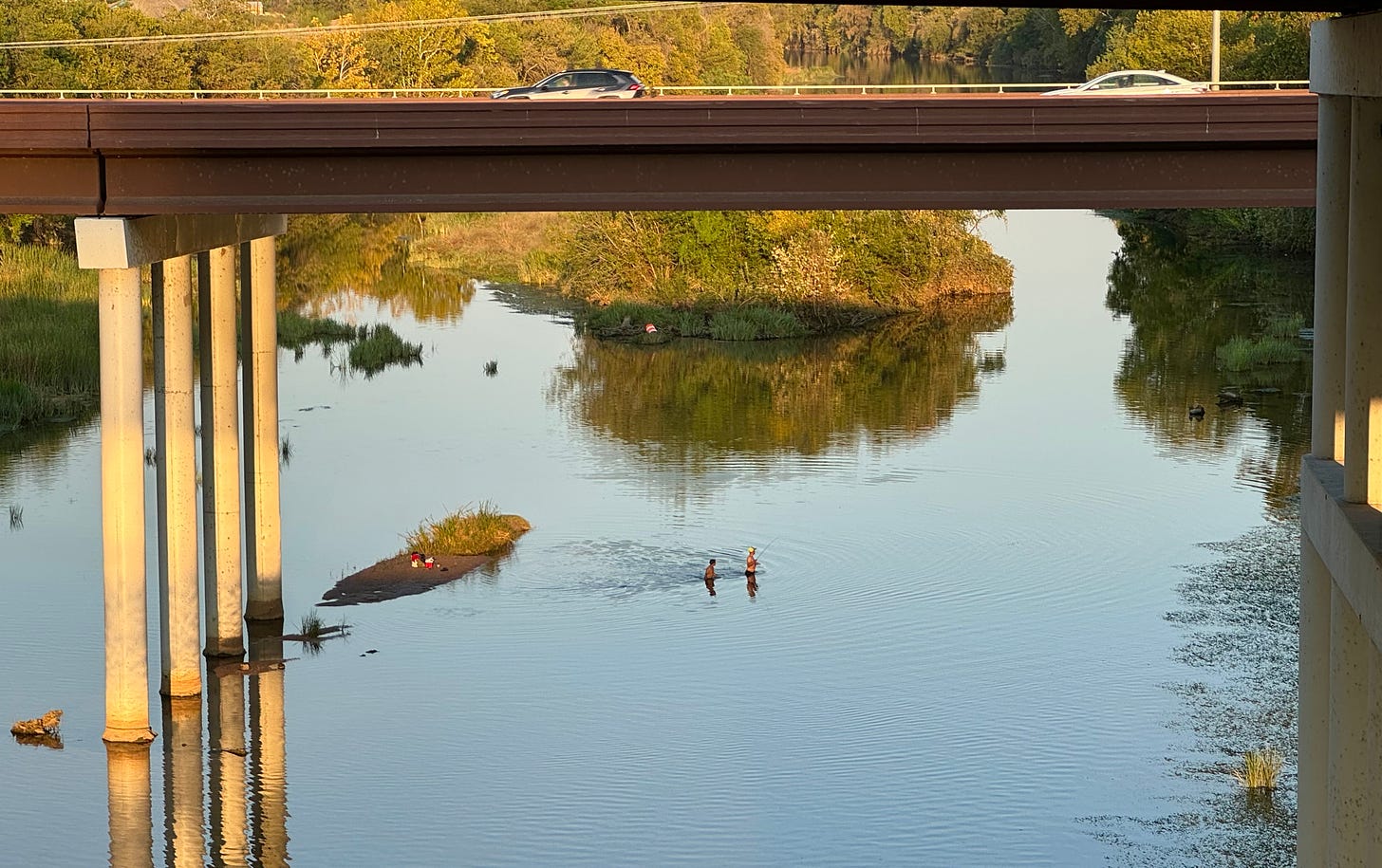 Dudes wading across the river under overpass bridge