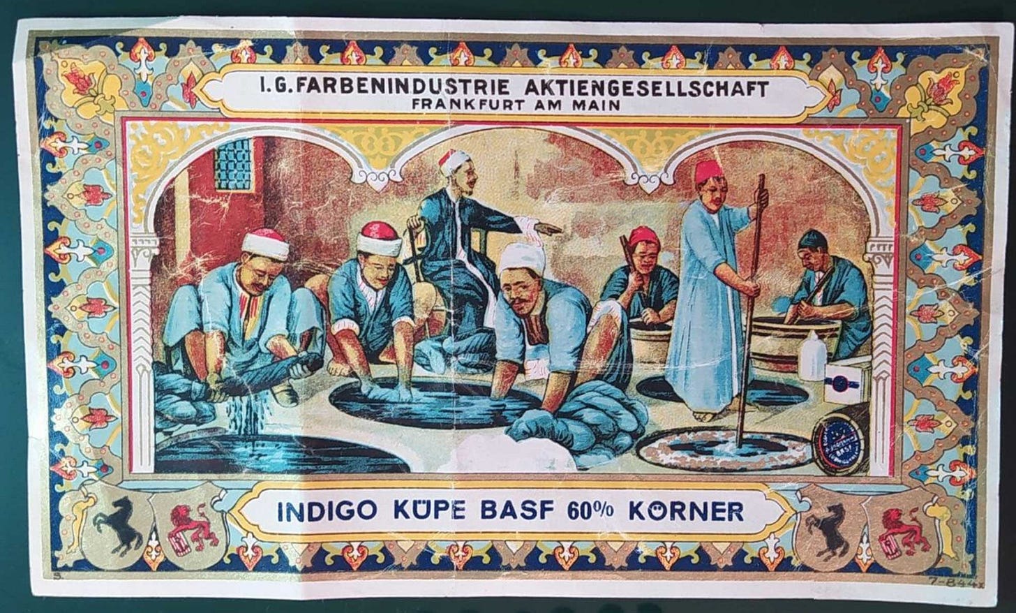 A richly decorated label with an ornate border featuring Middle Eastern-inspired patterns in blues, reds, and yellows. The central image depicts several persons, dressed in traditional garments and turbans, engaged in the process of indigo dyeing, stirring large vats of blue dye. Text at the top reads "I.G. FARBENINDUSTRIE AKTIENGESELLSCHAFT FRANKFURT AM MAIN" and at the bottom "INDIGO KÜPE BASF 60% KÖRNER," indicating the product and manufacturer. A richly decorated label with an ornate border featuring Middle Eastern-inspired patterns in blues, reds, and yellows. The central image depicts several persons, dressed in traditional garments and turbans, engaged in the process of indigo dyeing, stirring large vats of blue dye. Text at the top reads "I.G. FARBENINDUSTRIE AKTIENGESELLSCHAFT FRANKFURT AM MAIN" and at the bottom "INDIGO KÜPE BASF 60% KÖRNER," indicating the product and manufacturer.