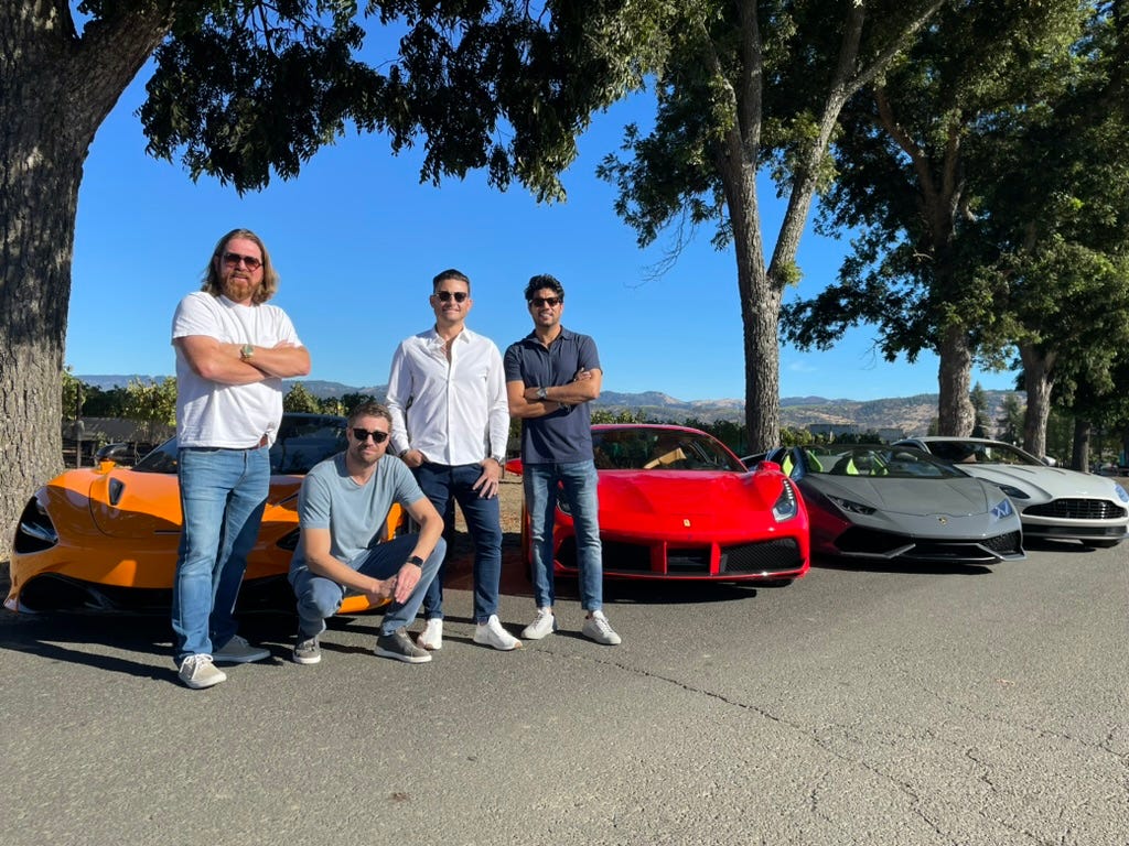 A group of men posing for a picture with cars

Description automatically generated