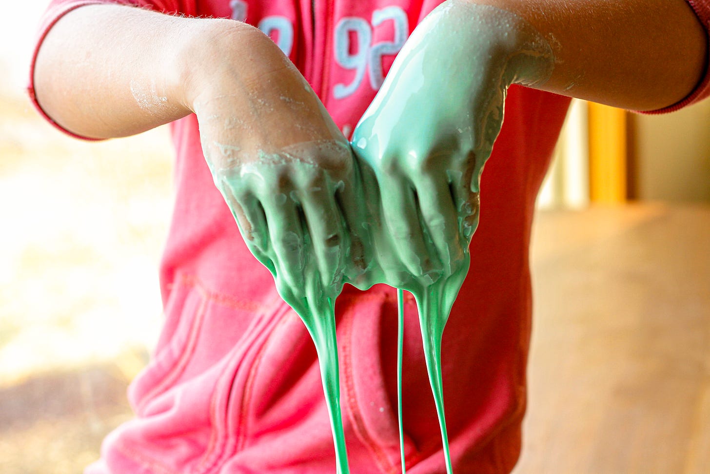 A green goo oozes off of a child's hands. Only the child's arms and torso in a red sweatshirt are visible.