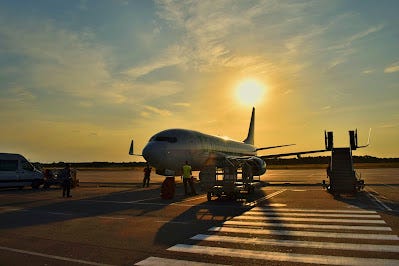 photo of a white aeroplane silhouetted by a sunset