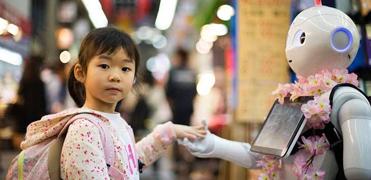 Photo of a young girl holding hands with a robot.