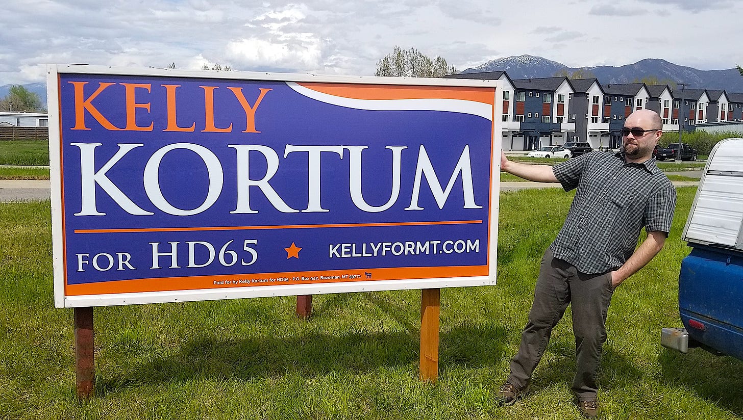 man standing next to large campaign sign outside
