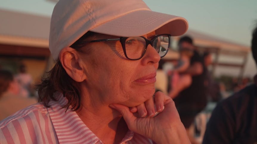 woman wearing a cap and black sunglasses looks contemplative among sunset glow