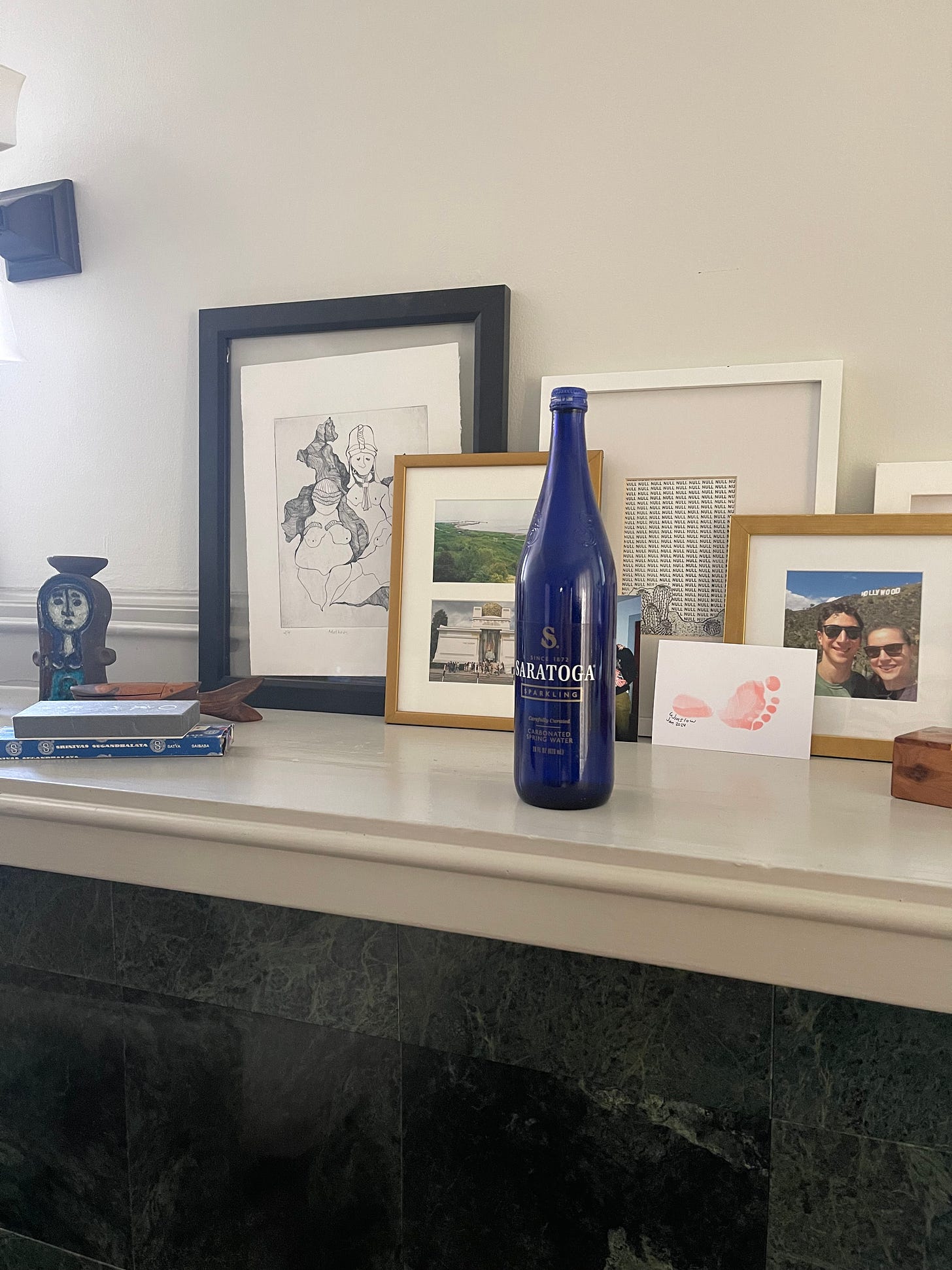 Saratoga Springs blue glass water bottle sitting atop a mantlepiece surrounded by framed art.