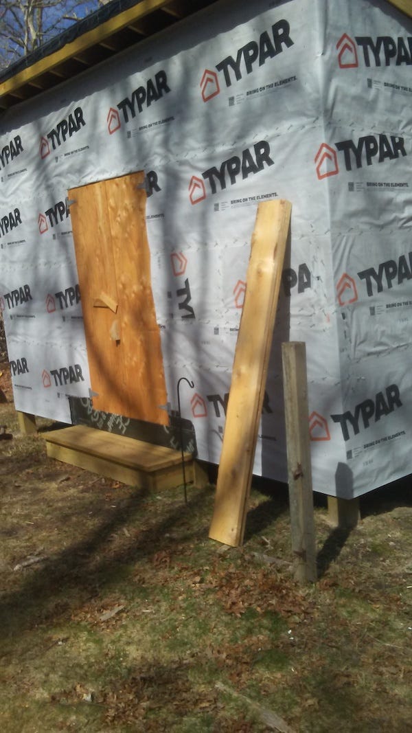 Photo of a big ol' shed with an unpainted plywood door, its walls covered in "Typar" paper