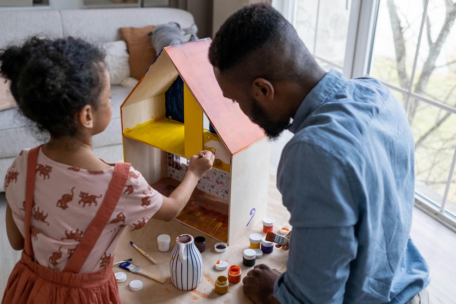 A father and daughter playing with a dollhouse
