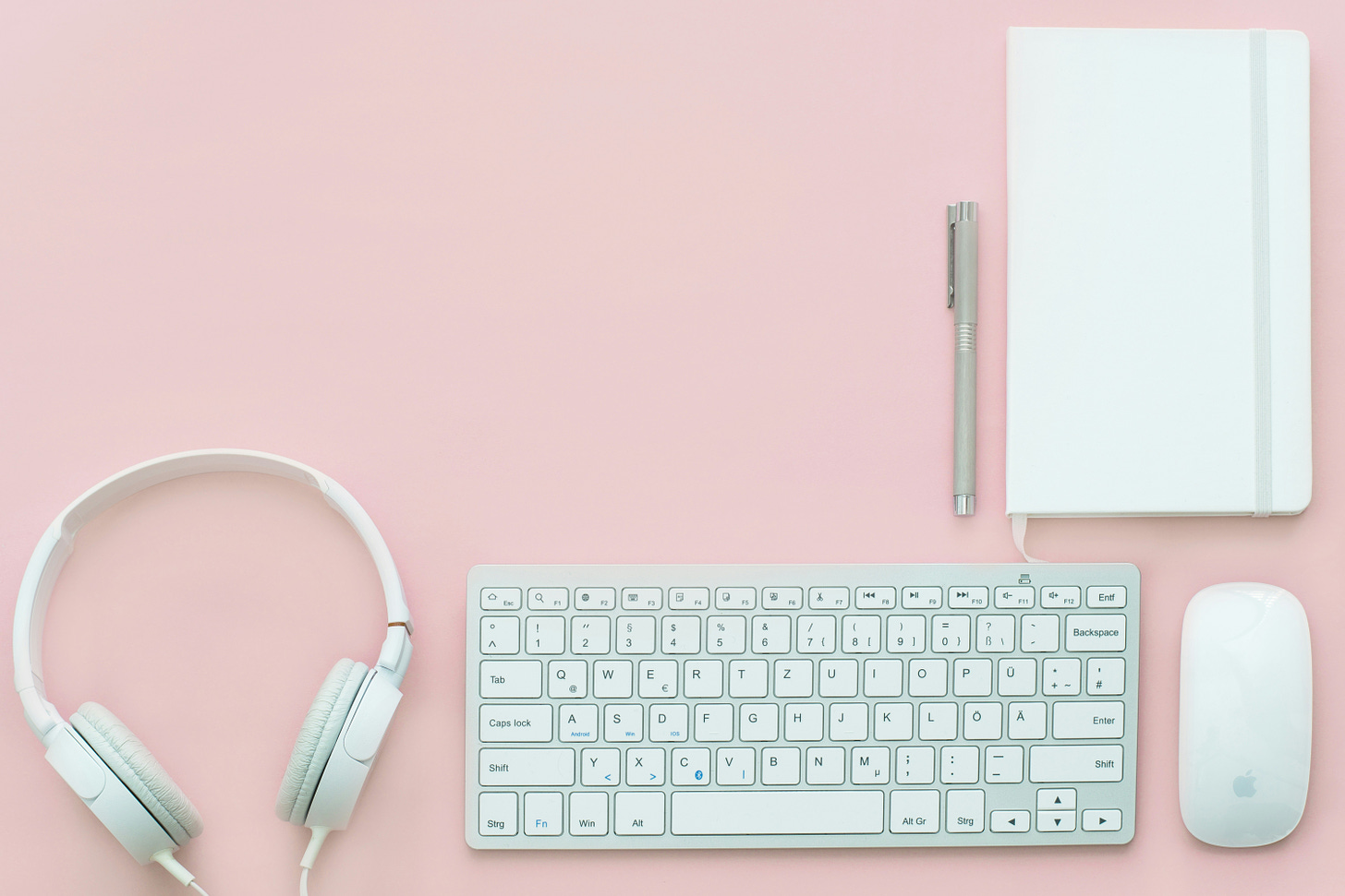 Headphones, keyboard, a notebook, and mouse all sit atop a pink surface.