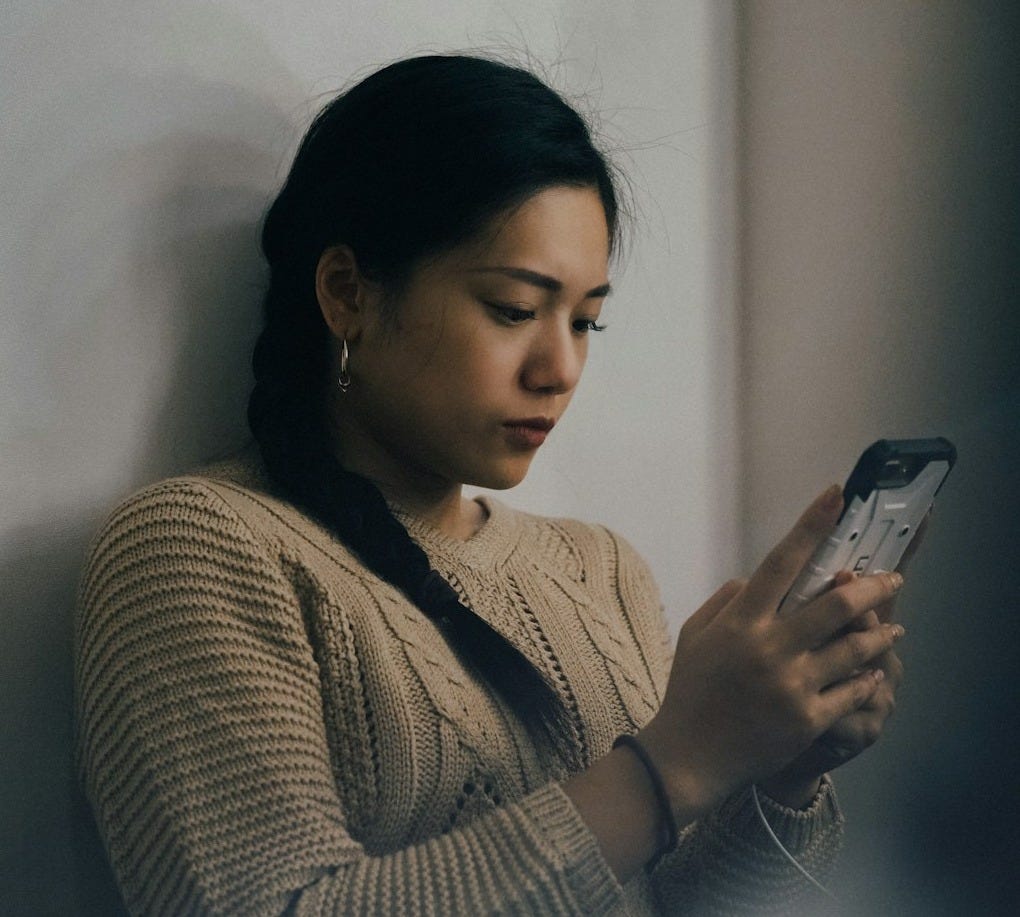 woman leaning back on white wall and using smartphone